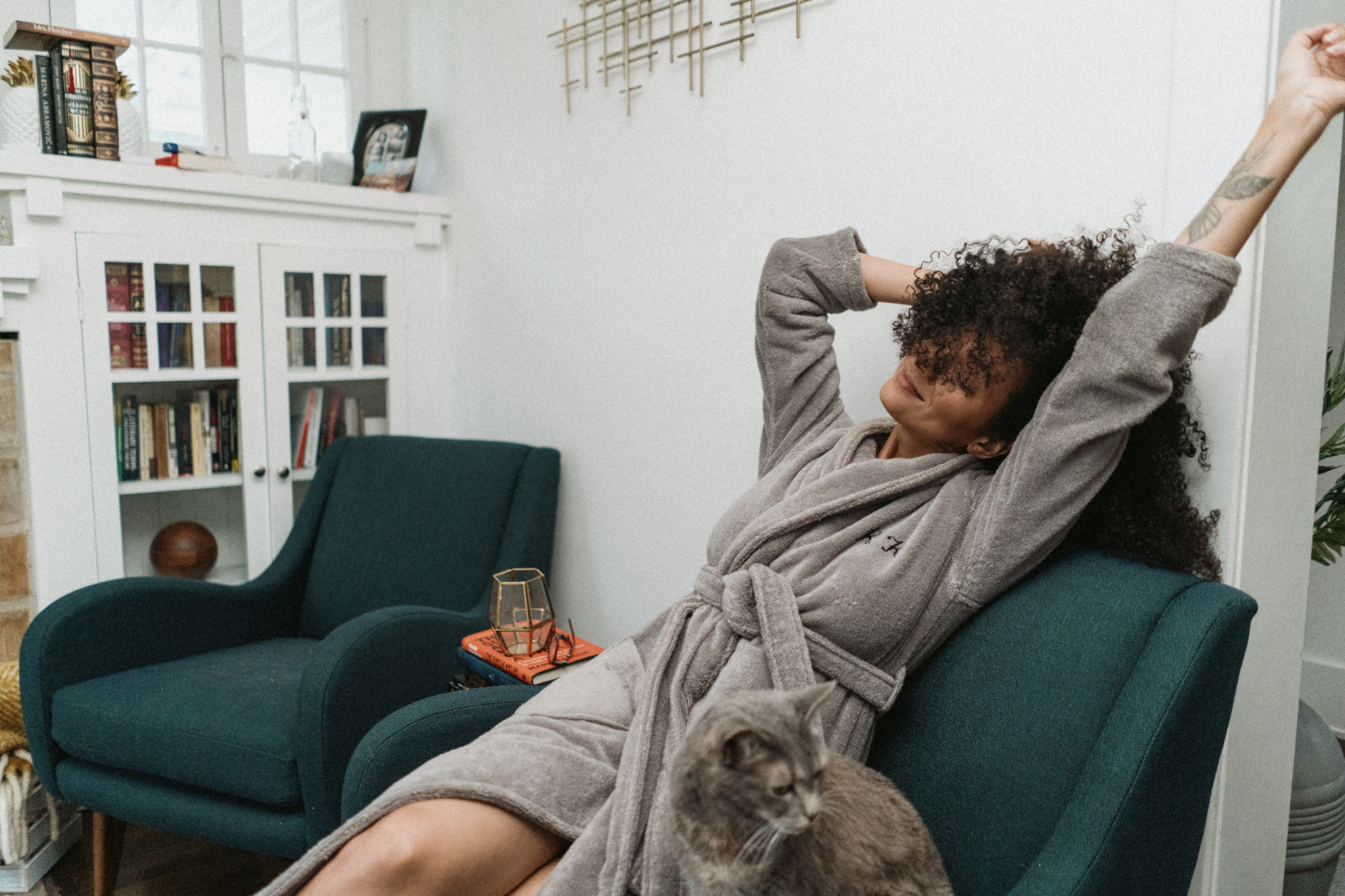 A woman wearing a robe, sitting in an armchair stretching, practicing self-love