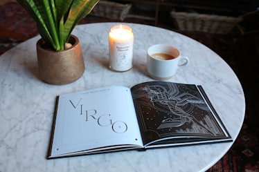 Birthdate Co.'s 'Birthdate Book' is opened up on a marble coffee table next to a celestial candle an...
