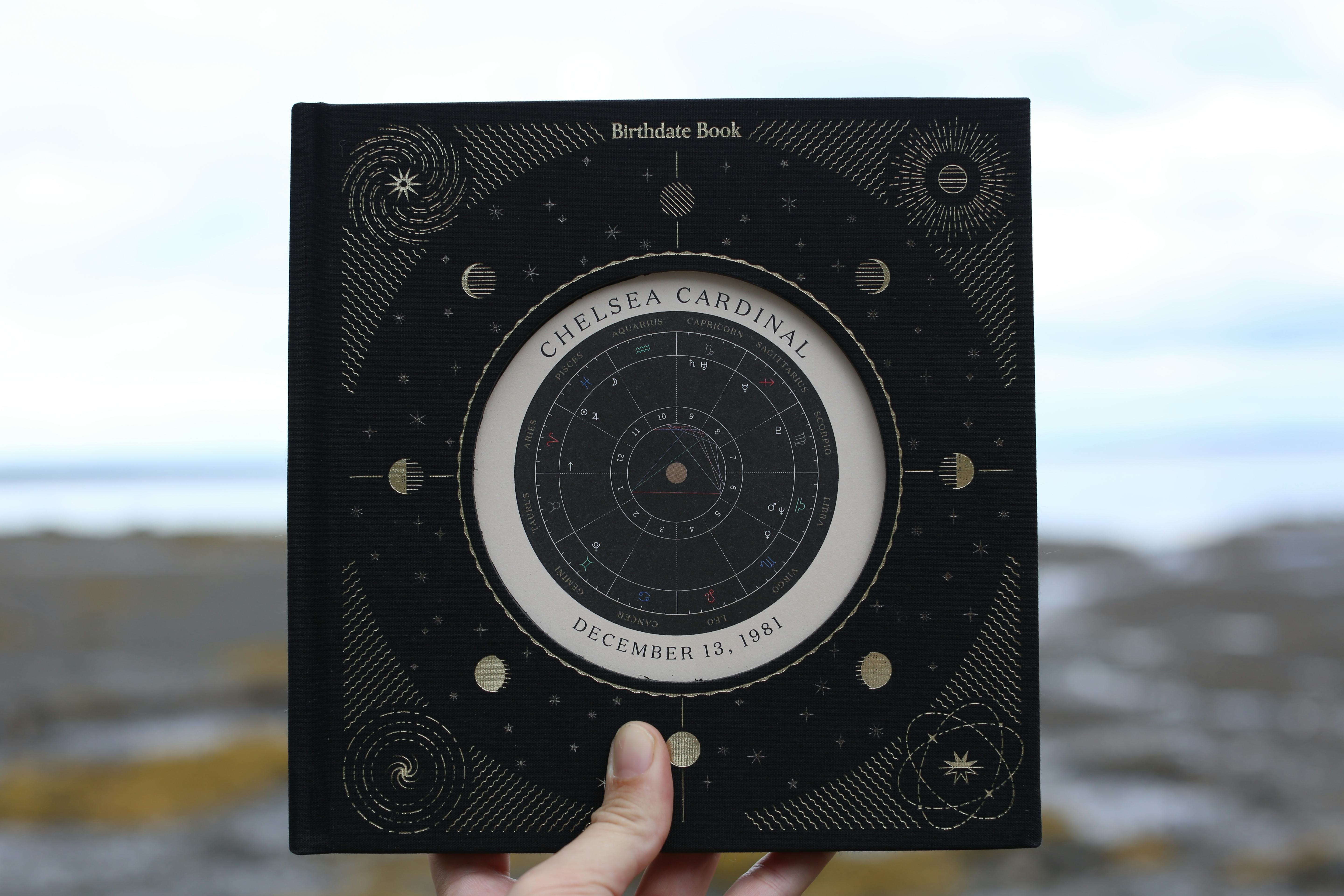 Birthdate Co.’s ‘Birthdate Book’ has a black hard cover with a shiny astrological illustration on th...