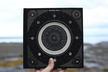 Birthdate Co.’s ‘Birthdate Book’ has a black hard cover with a shiny astrological illustration on th...