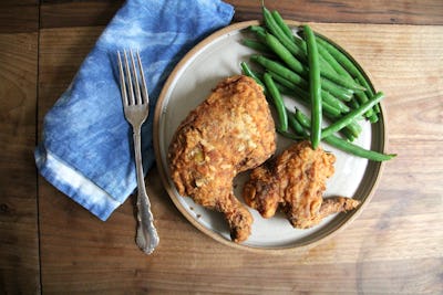 A plate with crunchy cried chicken and green beans with a fork and a blue napkin