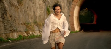 Harry Styles runs out of a tunnel, wearing a loose white button down, on the Amalfi Coast. 