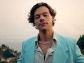 Harry Styles dressed in a teal suit, stands in front of the ocean on the Amalfi Coast. 