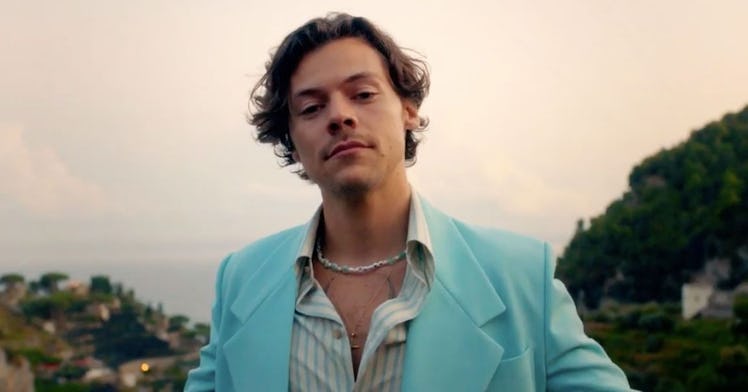 Harry Styles dressed in a teal suit, stands in front of the ocean on the Amalfi Coast.