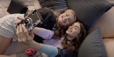Emily and Camille from Netflix's 'Emily in Paris' take an Instagram photo while laying on an art ins...