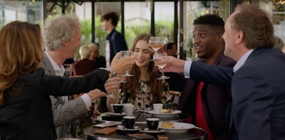 The marketing firm co-workers from 'Emily in Paris' sit at lunch and clink their drinks together.