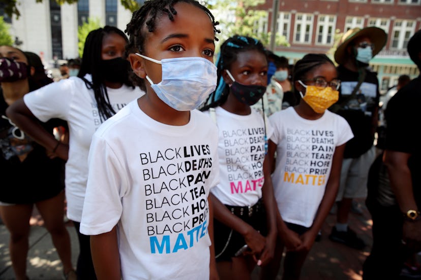  A boy and several other Black children wear face masks and white t shirts that say, "Black lives .....