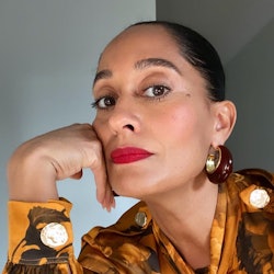 Tracee Ellis Ross posing with red lipstick, and an orange floral button up shirt