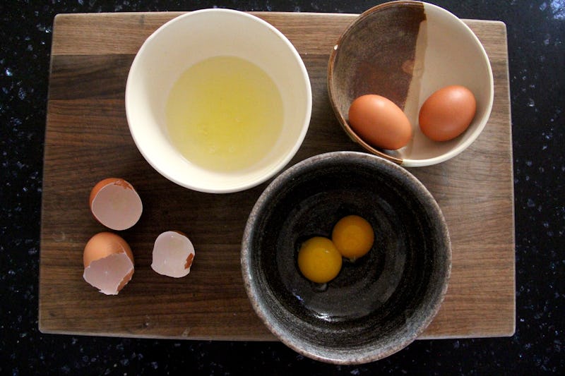 Egg whites, egg yolk and eggs separated into three bowls on a table 
