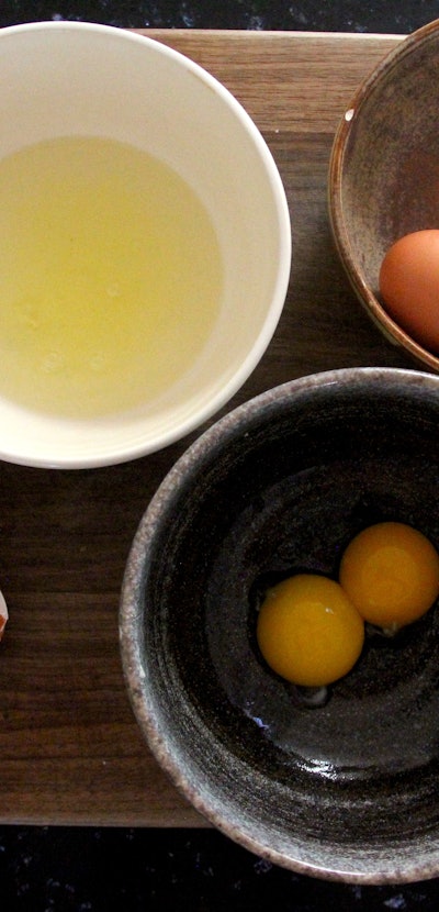 Egg whites, egg yolk and eggs separated into three bowls on a table 
