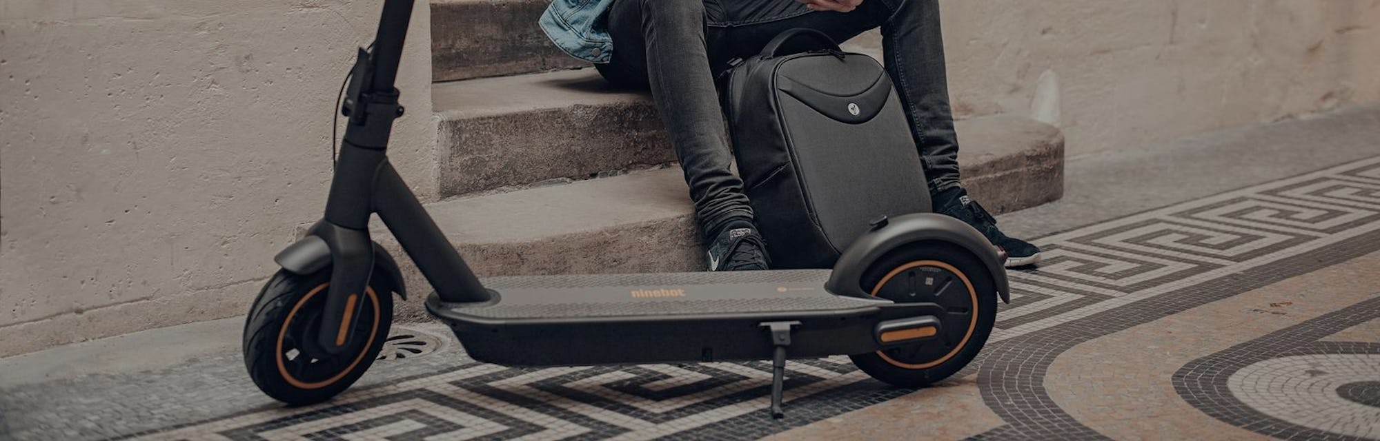 A man sitting next to a Segway Ninebot Kickscooter MAX.