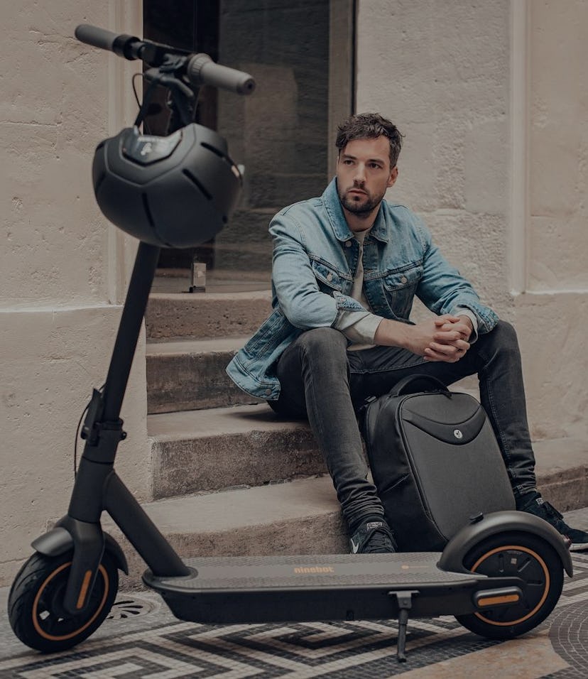 A man sitting next to a Segway Ninebot Kickscooter MAX.