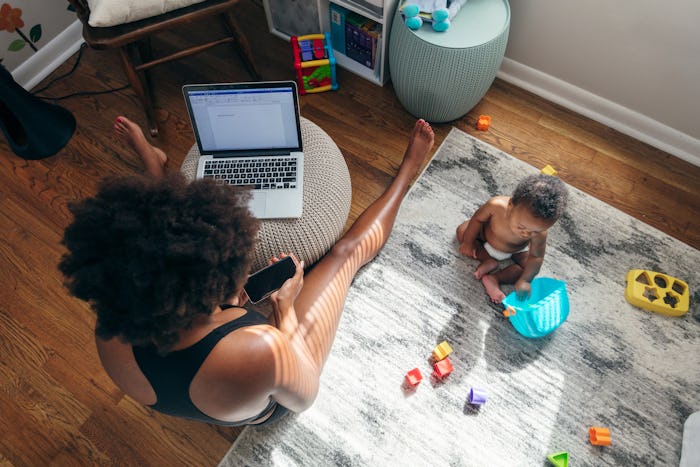 mom working on laptop next to toddler playing on floor