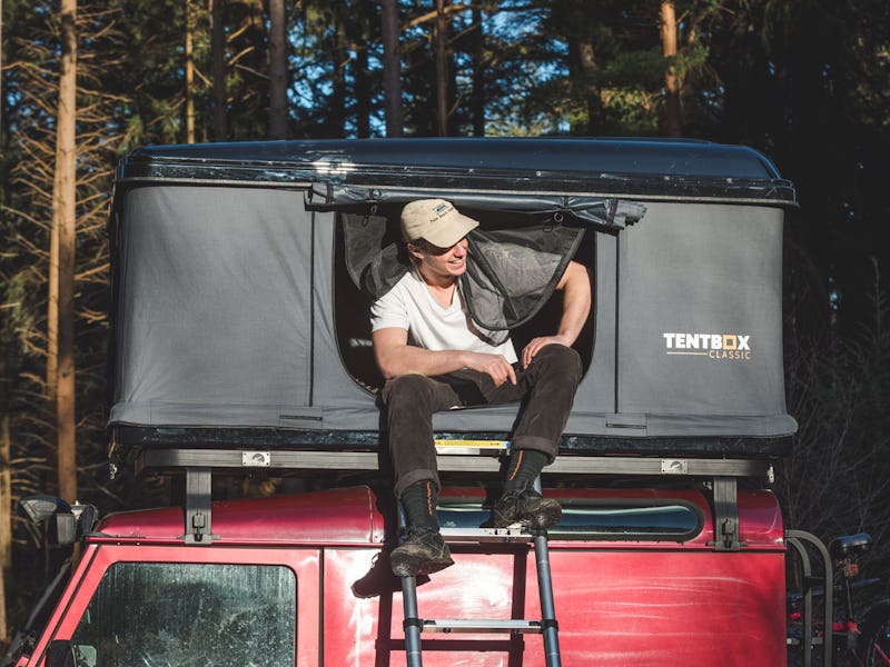 A person sits in a TentBox Classic with their feet on the ladder