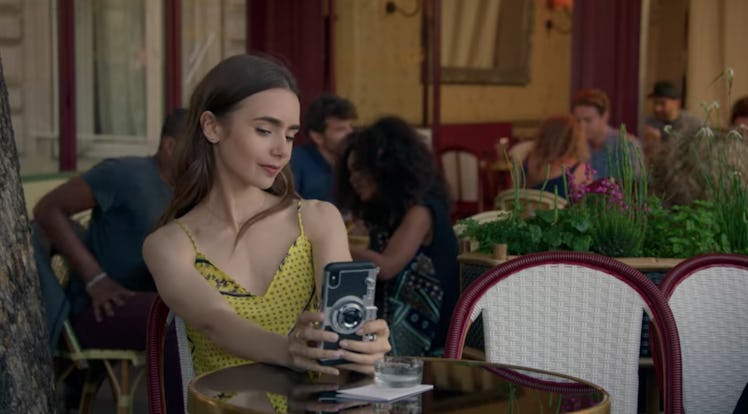 Emily (Lily Collins) sits in a cafe in Paris by herself with her phone. 