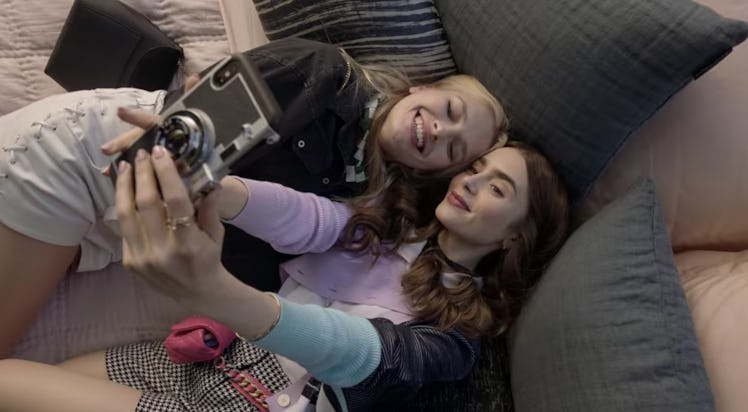 Emily (Lily Collins) and Camille (Camille Razat) pose for a selfie while lying in bed. 
