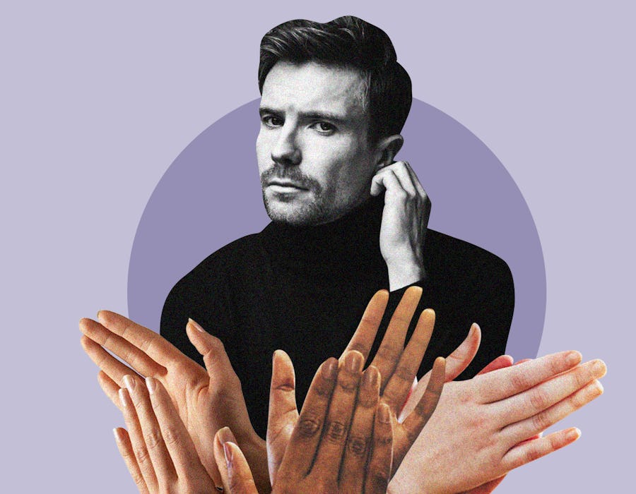 Joe Dempsie posing in a black turtleneck while a group of hands clap in front of him