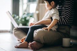 Child sits on mother's lap while she works on a laptop