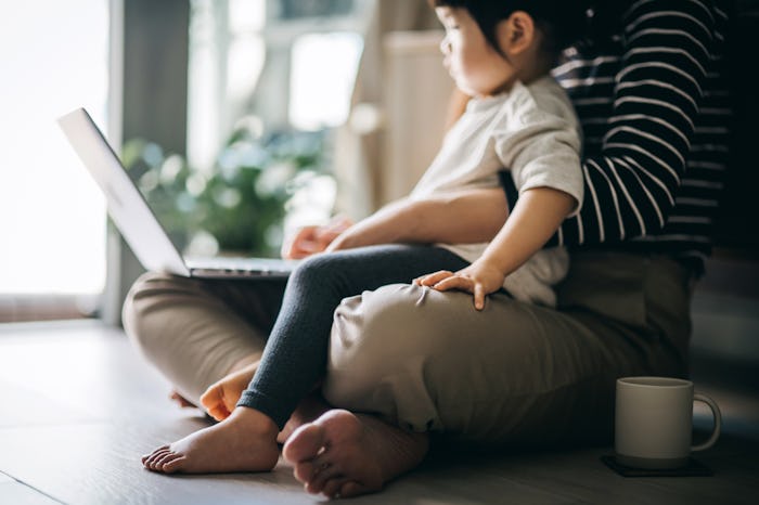 Child sits on mother's lap while she works on a laptop