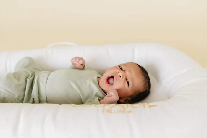 An image of a tiny newborn baby in a white Dock A Tot lounger.