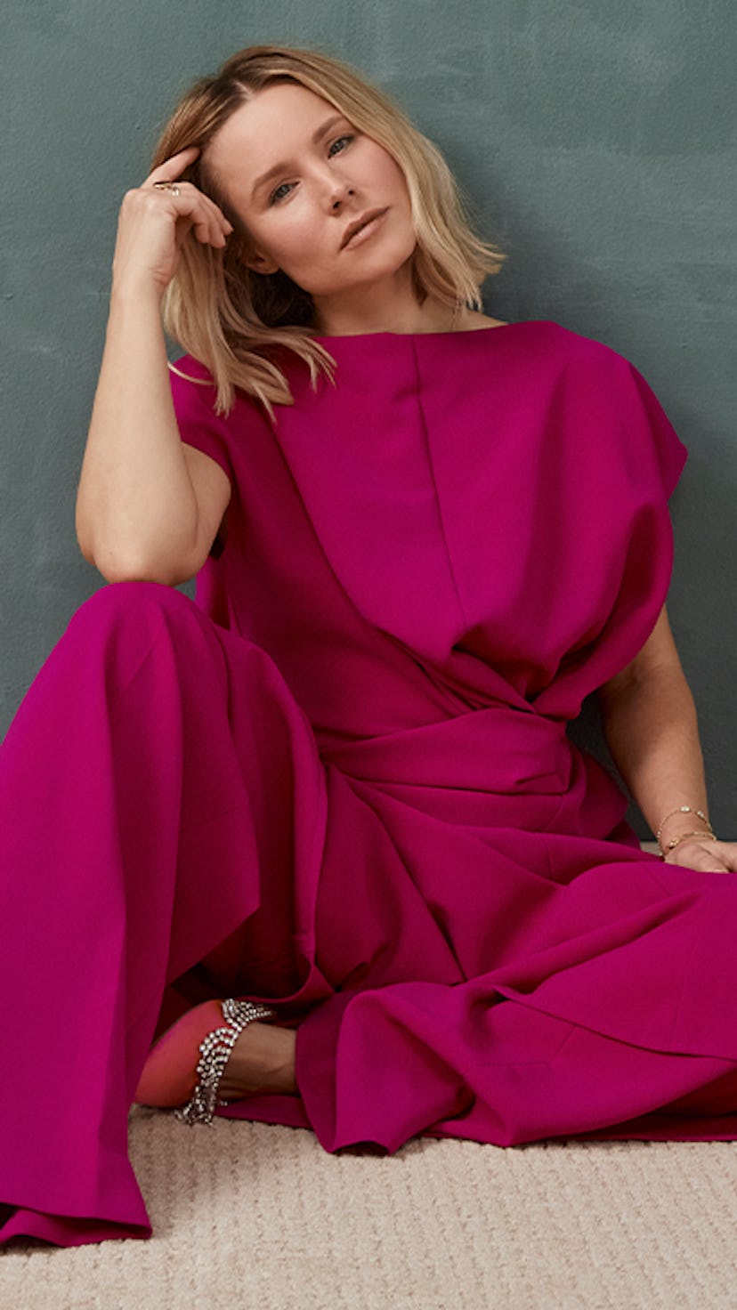 Kristen Bell posing on the floor in a magenta top and pants, with a pensive facial expression