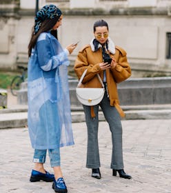 Two women stand outside, one is in a blue outfit the other in jeans and a suede jacket