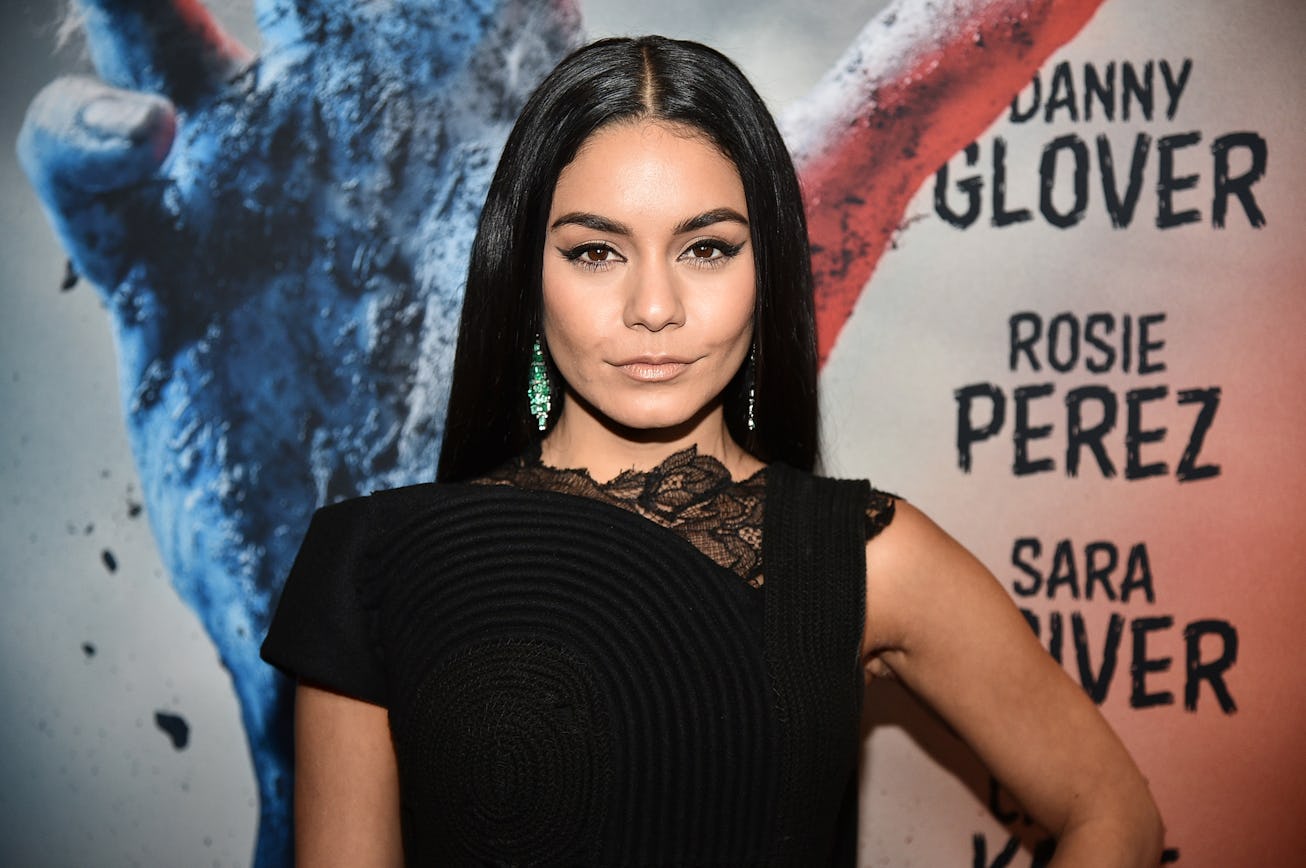 Vanessa Hudgens, with long brown hair that's parted down the middle, poses in a black dress on a red...