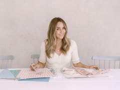 Lauren Conrad sits at a table with some fabric and pattern swatches. 
