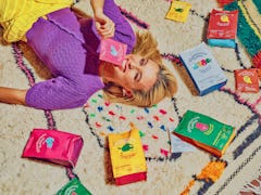 Emma Chamberlain lays amongst the Chamberlain Coffee products on a colorful rug.