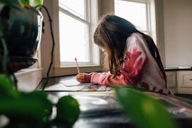Pre-teen girl with brunette hair is working on school work in the kitchen at home. Girl is wearing g...