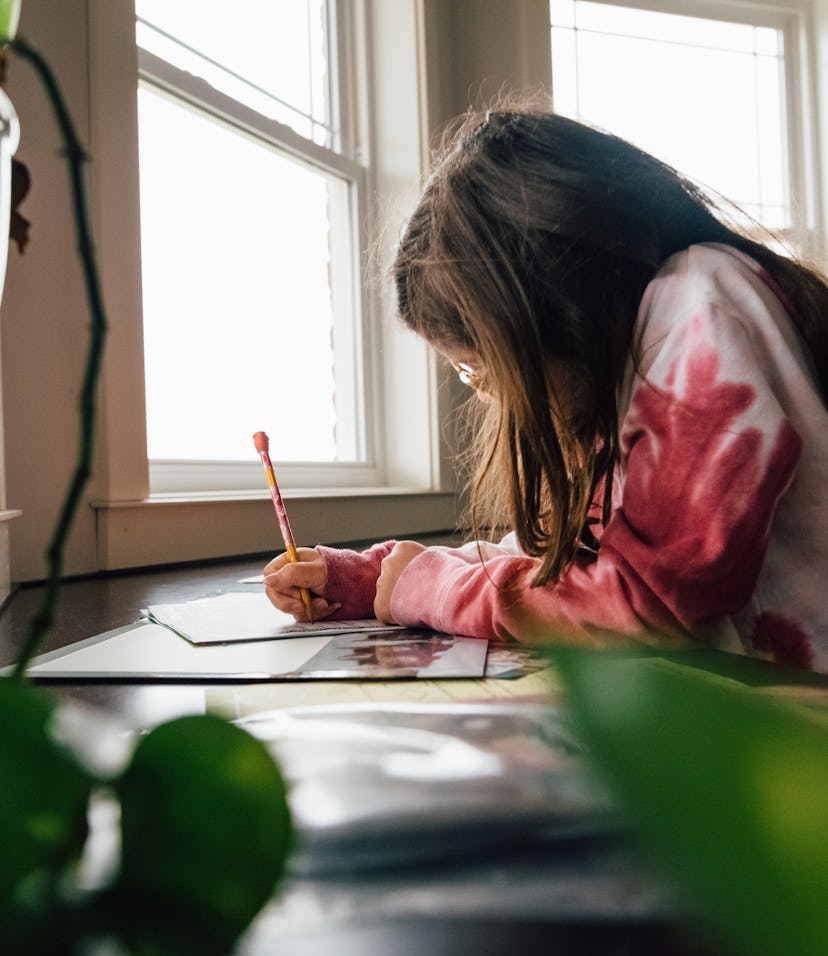 Pre-teen girl with brunette hair is working on school work in the kitchen at home. Girl is wearing g...