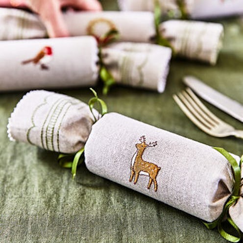 A  selection of christmas crackers covered in beige linen with embroidered deer and robin, on a gree...