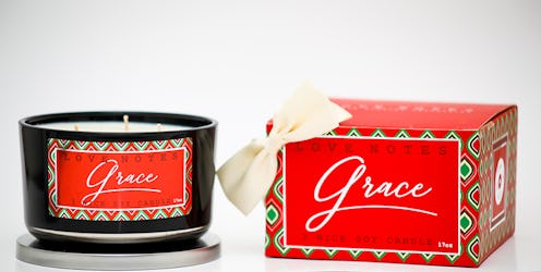 A three-wick candle with "grace" printed in white on red backing sits next to a gift box with a whit...