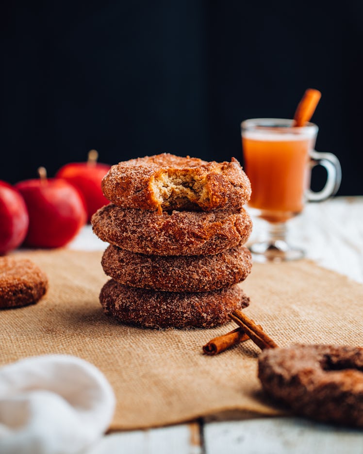 Julianna Vezza's apple cider donuts sit next to a glass of apple cider and fresh apples on a cloth.