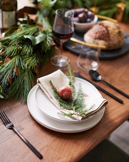 A tablescape featuring white plates, and pine tree leaves