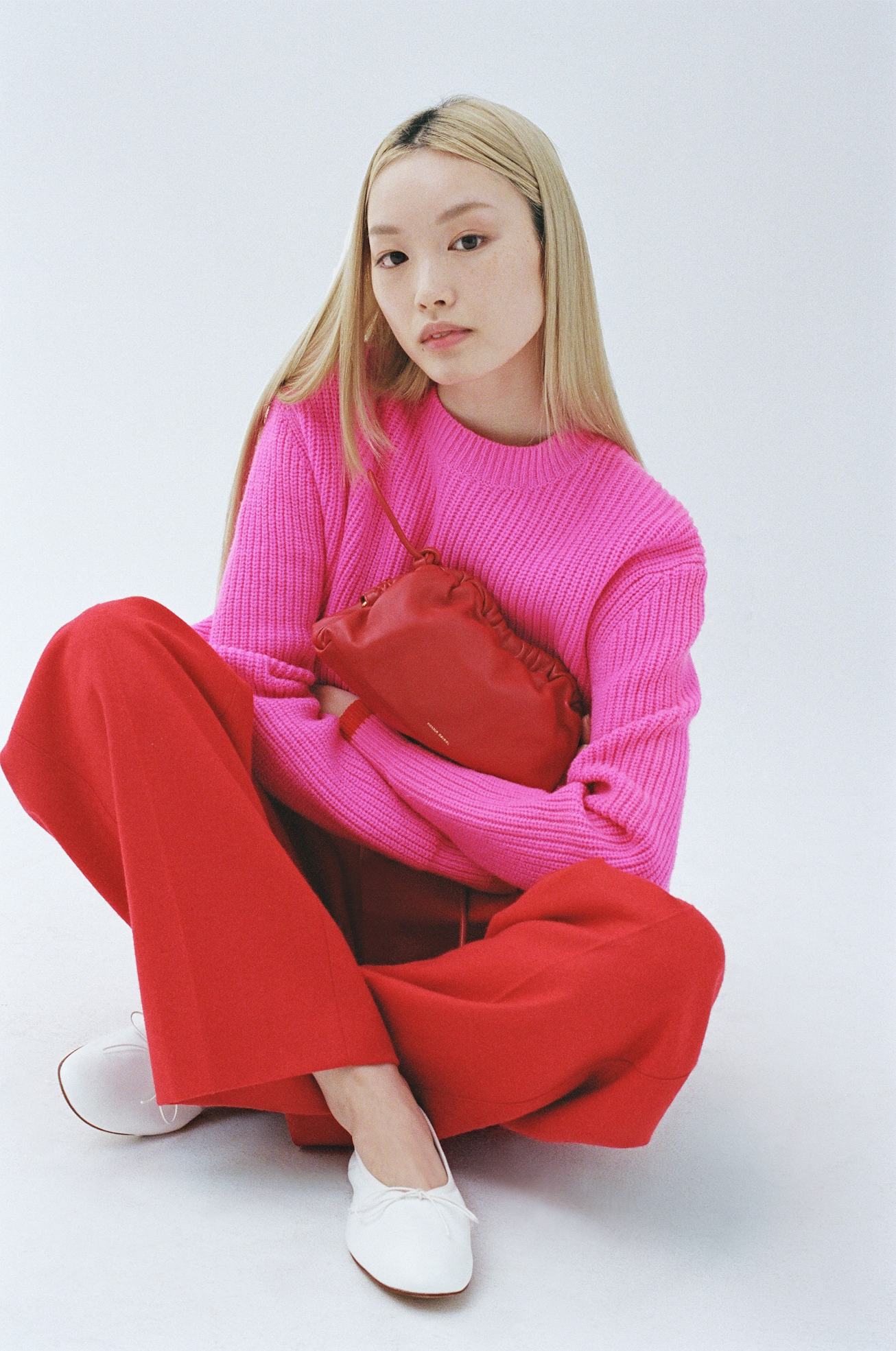 Australian fashion model Fernanda Ly sitting down wearing a pink sweater and red pants while holding...