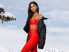 A young woman poses in red and black pieces from Alo Yoga against a wintery background.