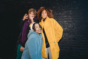 Three friends dancing in the city against a black brick wall