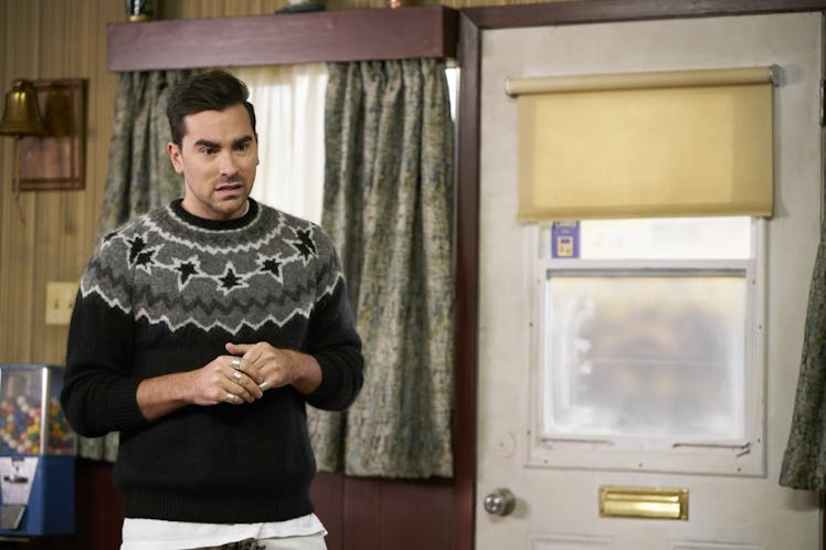 David Rose (Dan Levy) stands in the Schitt's Creek Motel wearing a black and grey sweater.