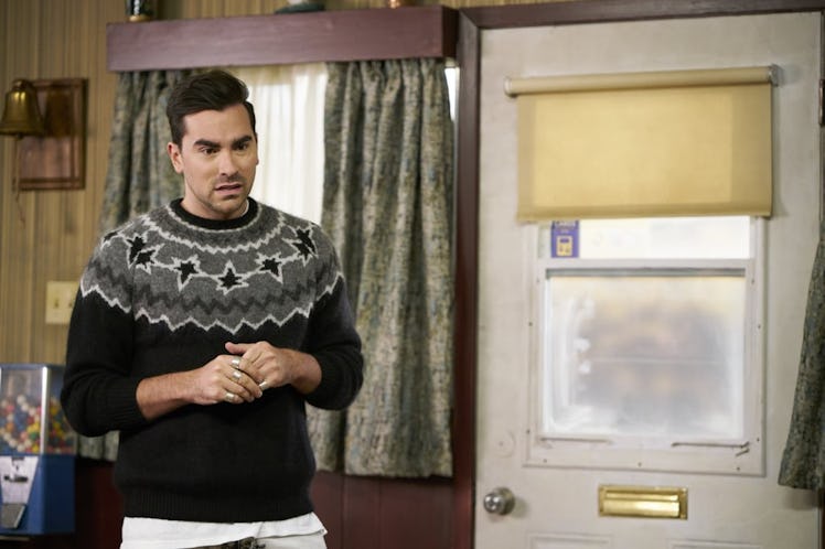 David Rose (Dan Levy) stands in the Schitt's Creek Motel wearing a black and grey sweater. 
