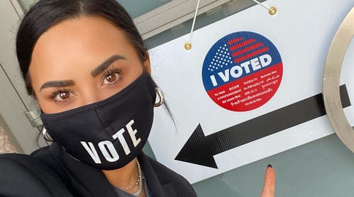 Demi Lovato taking a selfie with a black face mask with white "vote" sign on the mask