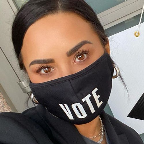 Demi Lovato taking a selfie with a black face mask with white "vote" sign on the mask
