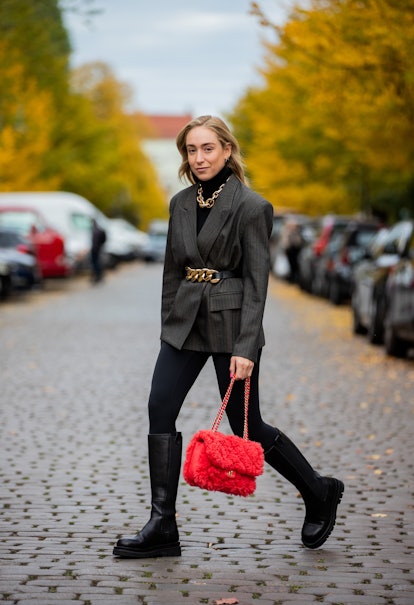 A woman in a black turtleneck, blazer, leggings and boots and a coral bag and a black-gold belt