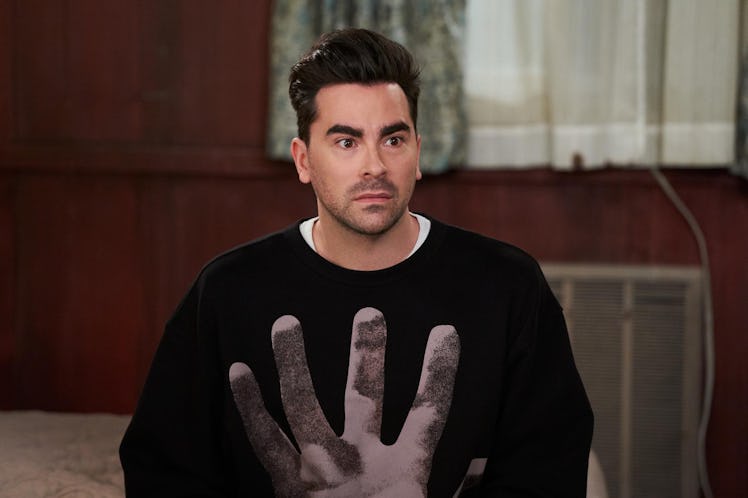 David Rose (Dan Levy) sits on a bed in the Schitt's Creek Motel. 