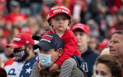 A child wearing a MAGA hat looks around at the crowd. She is sitting on her dad's shoulders.