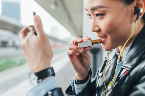 A woman doing her makeup while looking in a pocket mirror on a train station