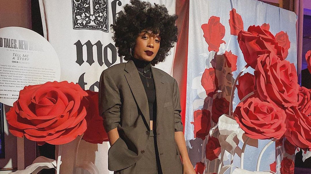 Young lady with curly hair posing in a dark green oversized suit
