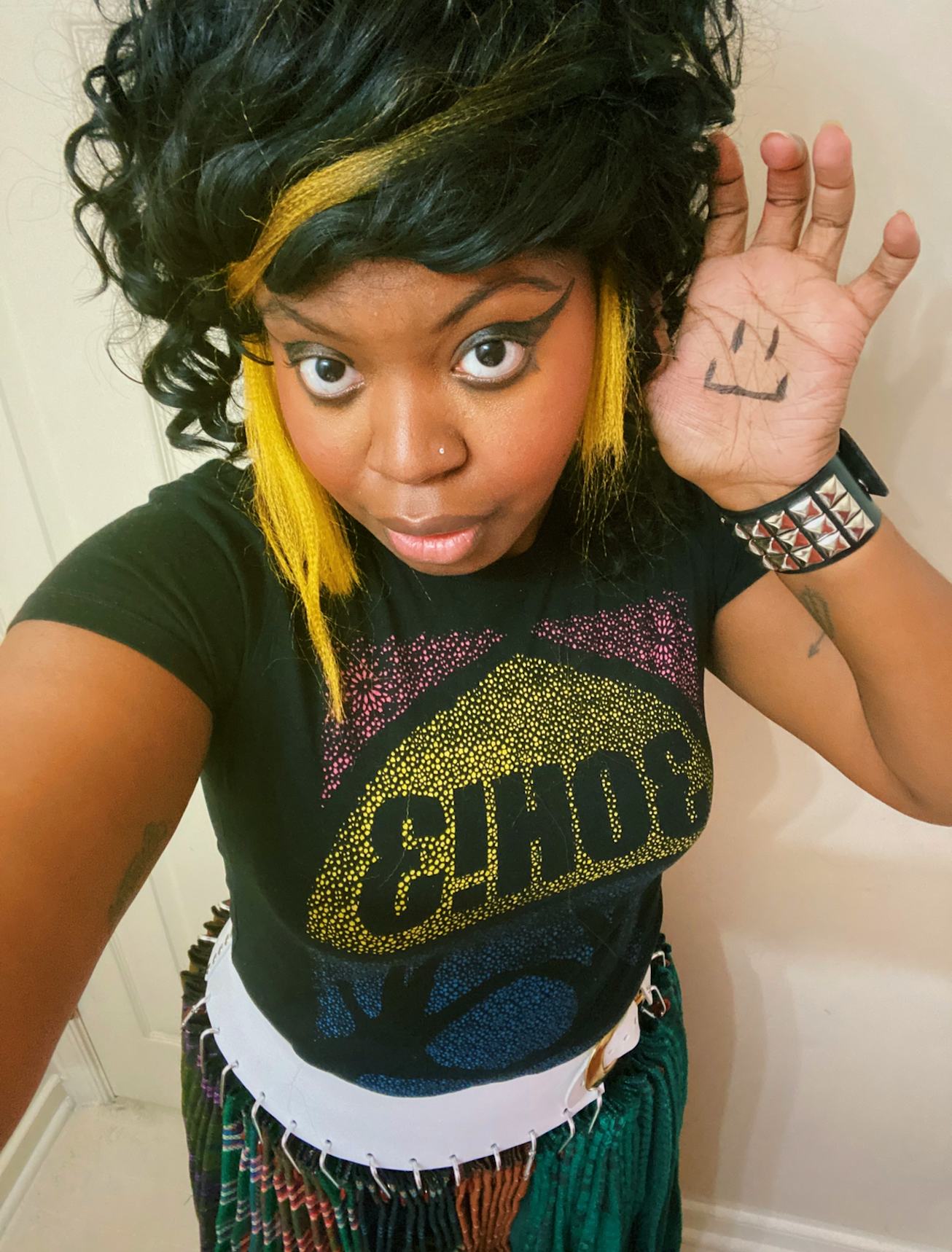 Singer Simpson waving to the camera with a smiley on her hand and yellow streaks in her hair