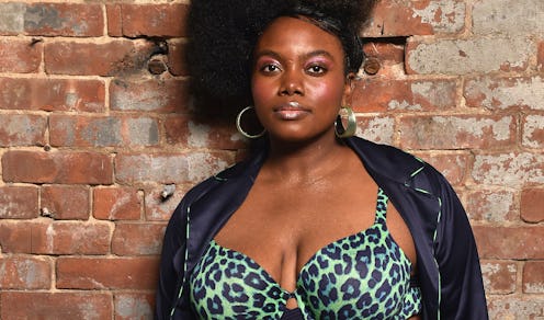 A plus-size model in a leather jacket and a green leopard print bra standing in front of a brick wal...