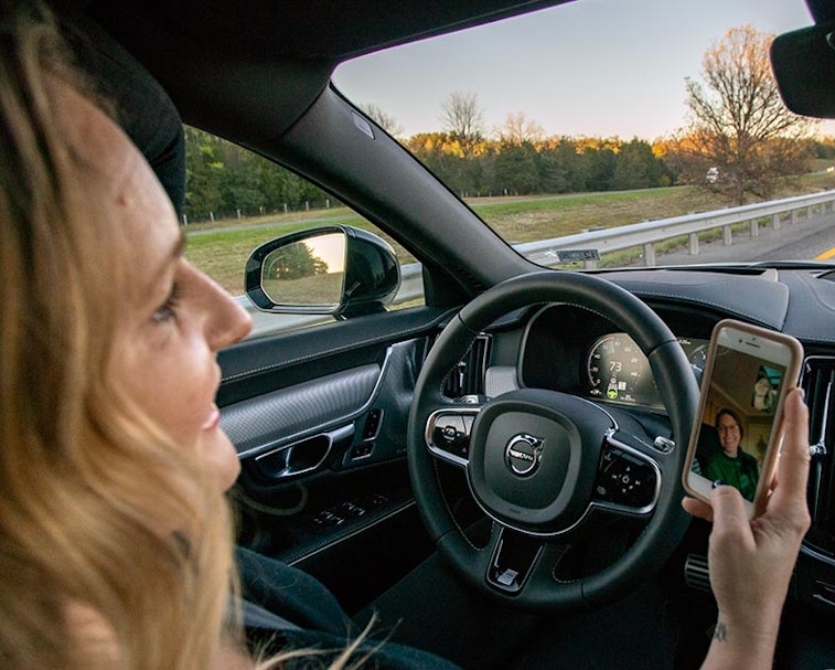 A person behind the wheel of a Volvo S90 Facetiming on their phone,